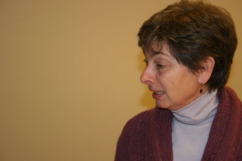 a woman in profile wearing a sweater and turtleneck against a plain wall