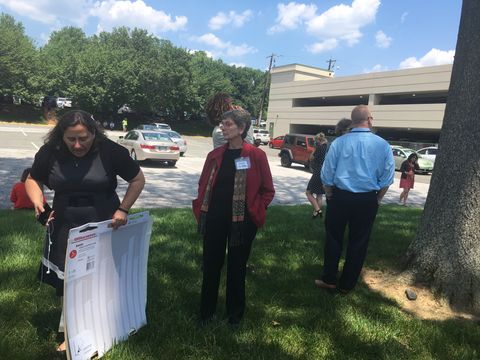 several people stand on grass near a parking lot and building on a sunny day