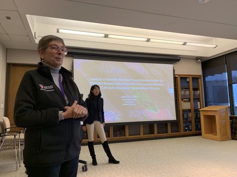 two women stand in a lecture room in front of a projected presentation slide