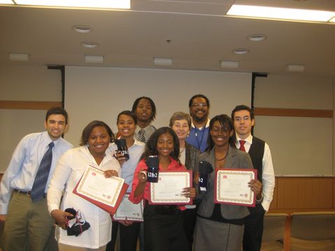 a group of people posing indoors with certificates and awards in a classroom or conference room