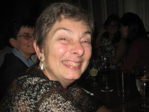 a smiling woman at a dimly lit table with drinks and other people in the background