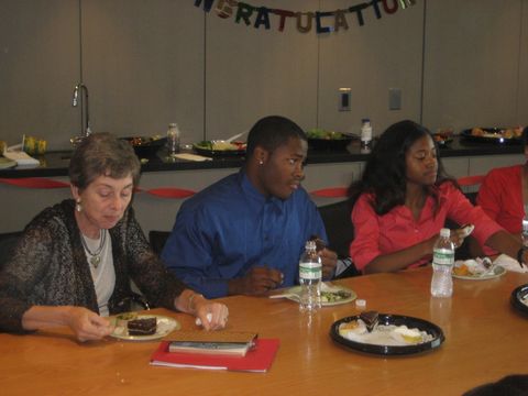 people sit at a table eating cake at a celebration indoors
