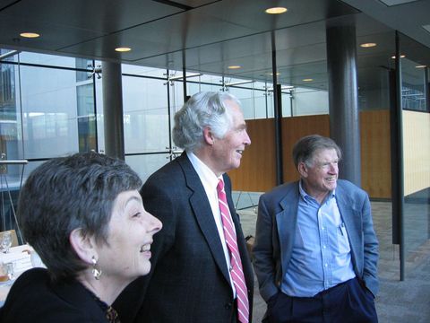 Three people in business attire conversing in a modern glass-walled office lobby.